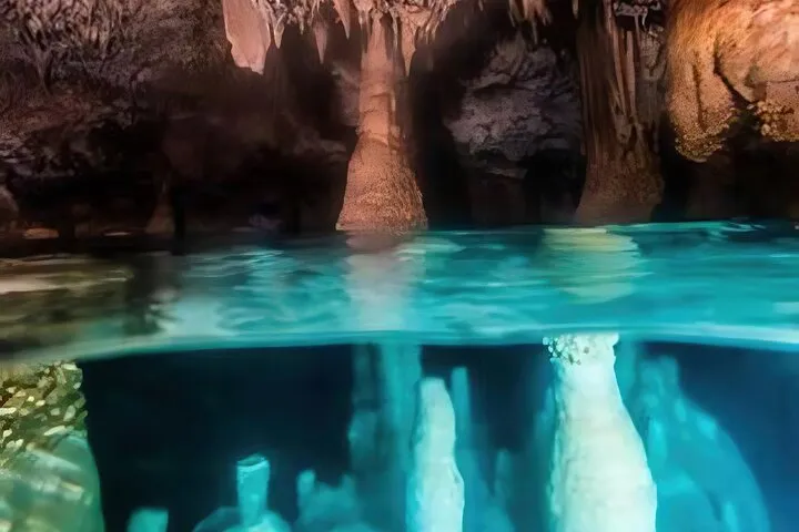 Guide with a flashlight beside a flooded limestone cave chamber on a Bonaire cave snorkeling tour